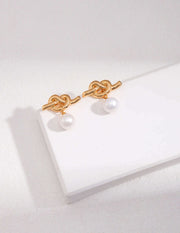 A pair of Intertwined Natural Pearl Drop Earrings on a white surface.