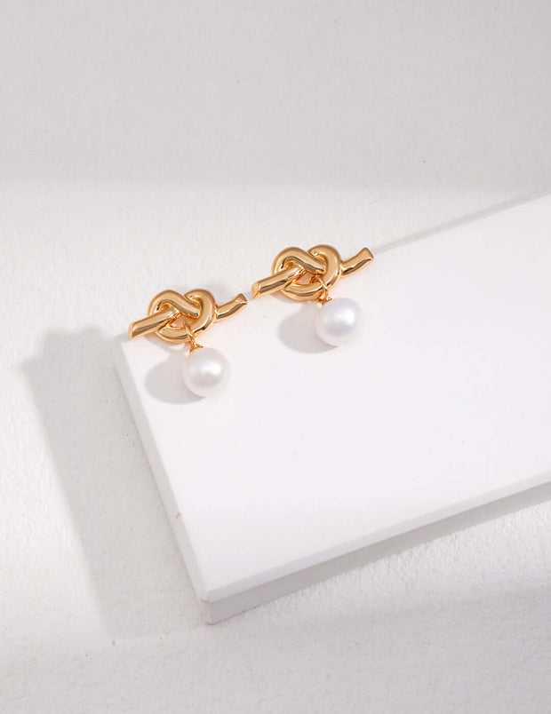 A pair of Intertwined Natural Pearl Drop Earrings on a white surface.