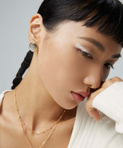 A woman wearing a white sweater and gold earrings with Eclipse Earrings.