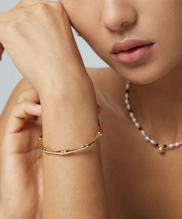 A woman showcasing her style with a Bamboo Bangle and pearls jewelry.