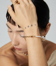 A woman wearing an elegant Tiger's Eye Pearl bracelet adorned with a stylish tattoo.