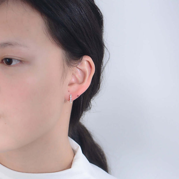 A stylish woman wearing a white shirt and a pair of Venus Huggie Hoop Earrings.