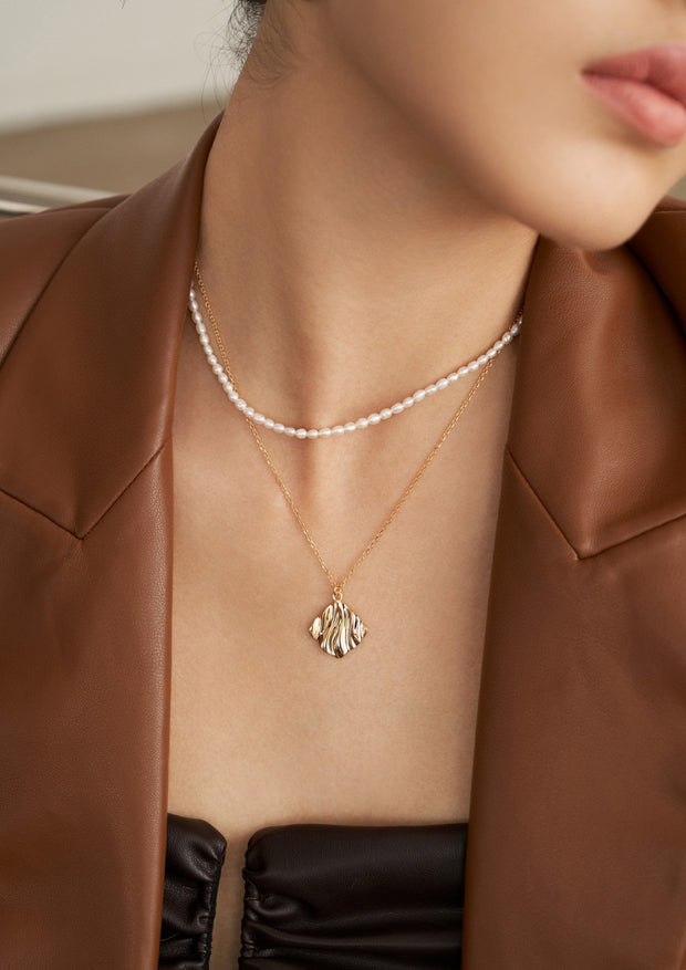 A fashion-forward woman donning a stylish brown jacket elegantly accessorized with a Natural Pearl Double Layered Necklace.