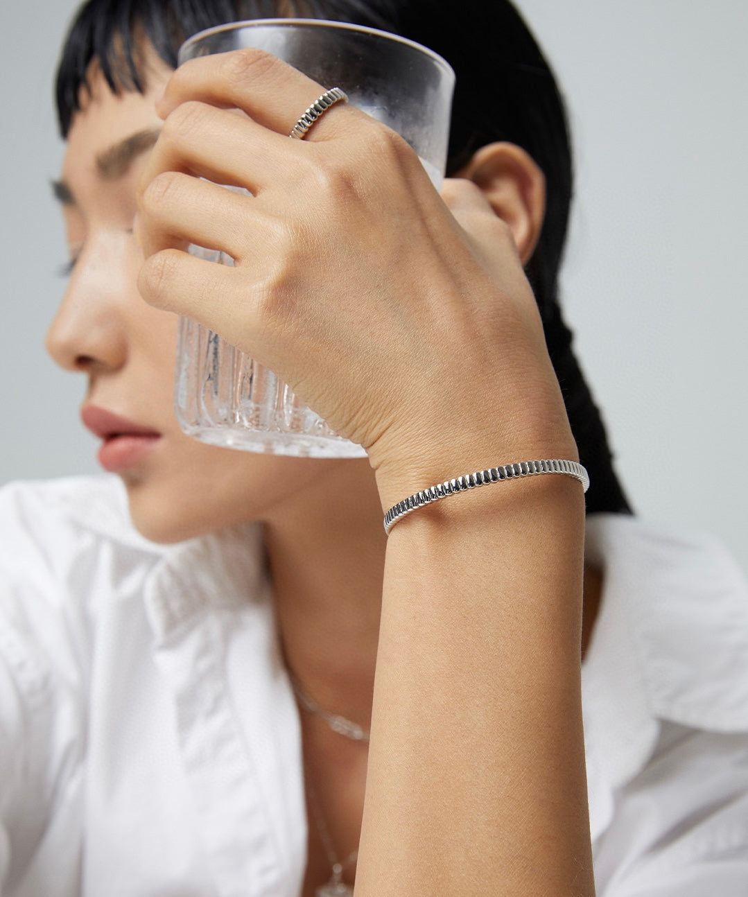 A Parisian woman is adorned with a statement accessory, the Parisian Gridline Bangle, as she holds a glass.