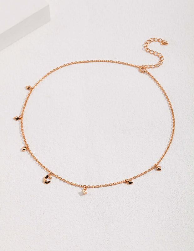 An 18K rose gold choker adorned with small charms, featuring the Starry Night Crescent Moon Necklace and creating a star-kissed look.