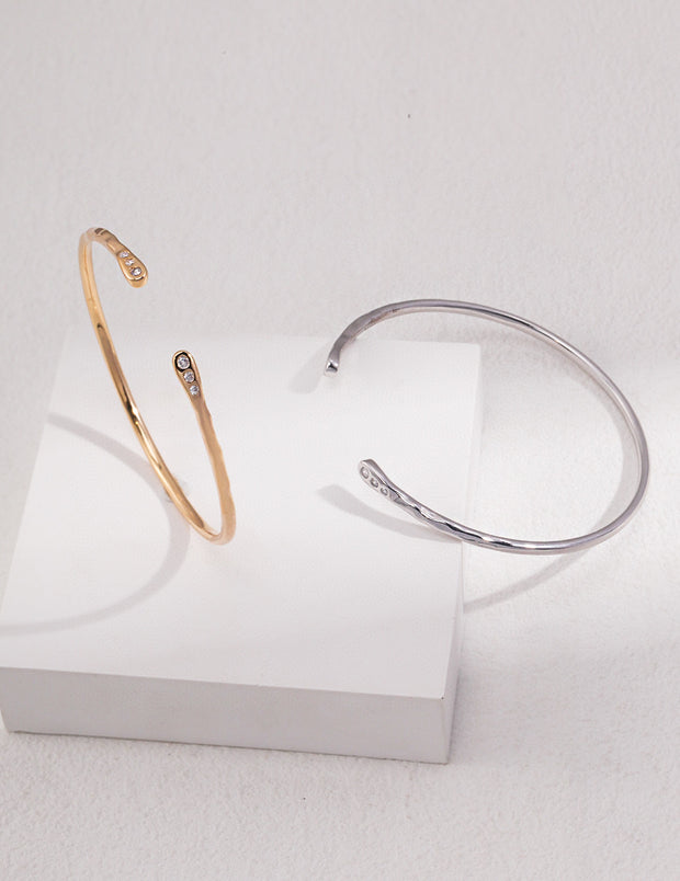 Two Minimalist Chic Bangles in gold and silver on a white surface, creating a timeless and chic look.