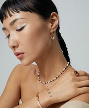 A woman wearing a Tigerite Charm Choker necklace with pearls, showcasing the Tigerite Charm Choker beauty and a tattoo on her arm.