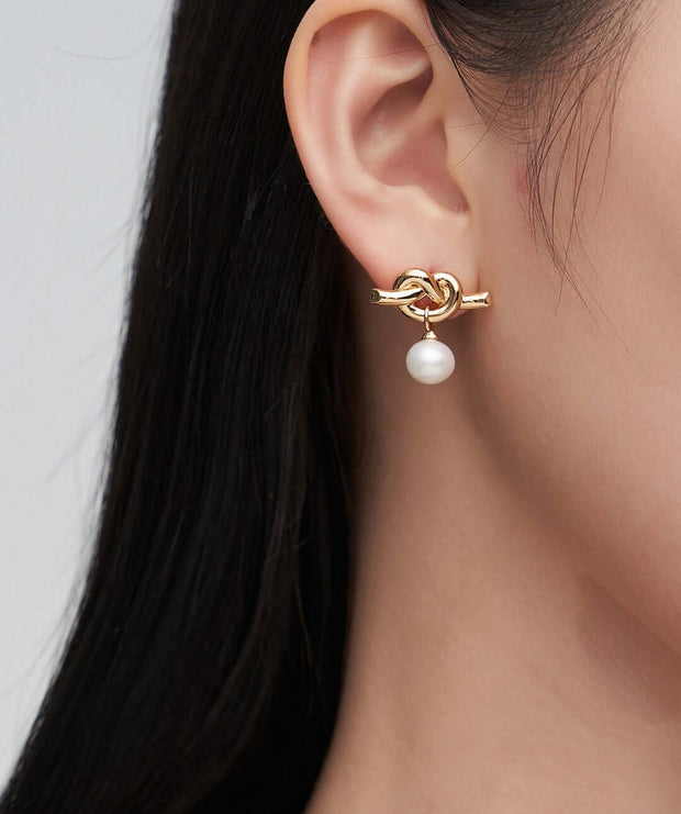 A woman wearing a pair of Intertwined Natural Pearl Drop Earrings.