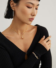 A woman wearing a black sweater, gold necklace, and Lunar Mist Bangle.