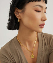 A woman adorned with a beautiful 18K gold necklace and Stylish Hoop Earrings.