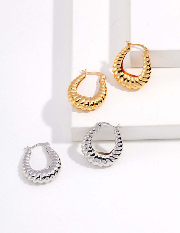 Three stylish hoop earrings on a white surface.